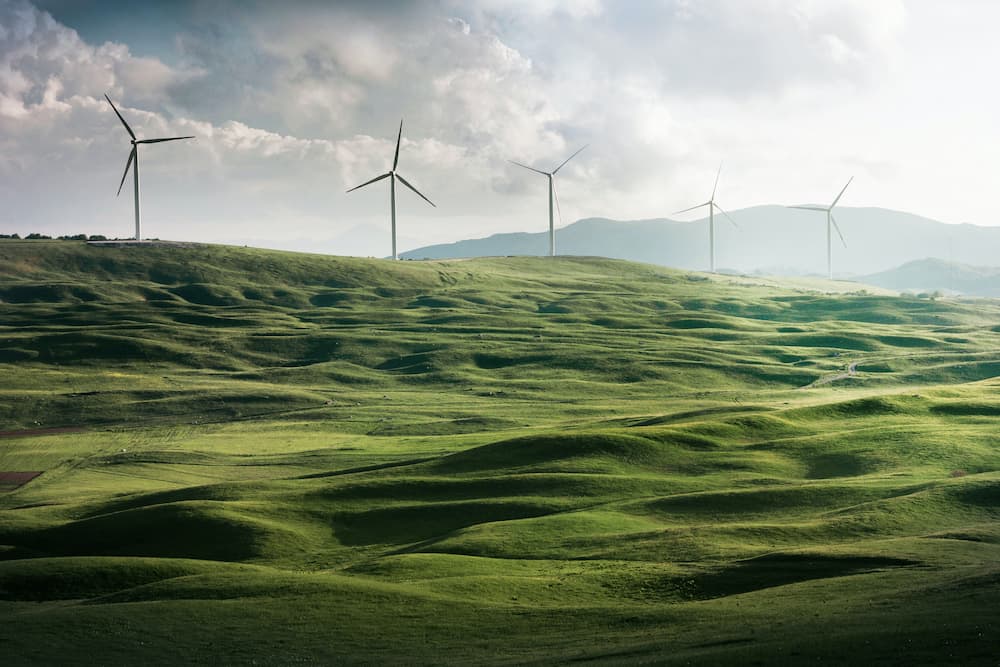 Paesaggio di colline verdi con turbine eoliche che generano energia pulita.